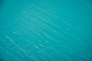 Obraz premium Texture of azure calm water of mountain lake. Meditative ripples on water surface. Nature minimal background of turquoise lake. Natural backdrop of clear cyan water. Full frame of lake fragment.