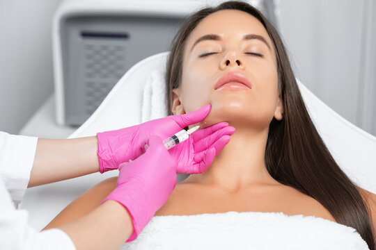 Cosmetologist makes lipolytic injections to burn fat on the chin, cheeks and neck of a woman against double chin. Female aesthetic cosmetology in a beauty salon.Cosmetology concept.