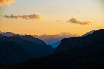 Colorful dawn landscape with beautiful blue mountains silhouettes and golden gradient sky with clouds. Vivid mountain scenery with picturesque multicolor sunset. Scenic sunrise view to mountain range.