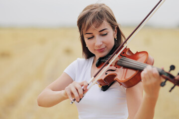 Beautiful romantic girl with loose hair playing the violin in the field.