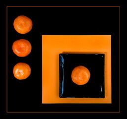 Composition of orange mandarin and black square plate on an orange table.
