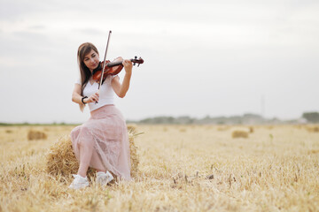 Beautiful romantic girl with loose hair playing the violin in the field.