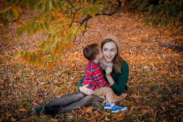 Happy young mother playing and having fun with her little baby son on sunshine warm autumn day in the park. Happy family concept