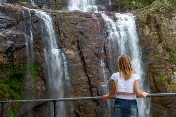 A girl stands in front of a waterfall and admires the beautiful view