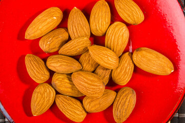 Almonds nuts in a red saucer on a bamboo mat, closeup