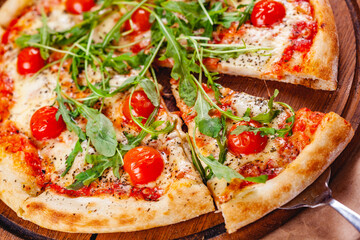 Italian Pizza with tomatoes, mozzarella cheese and arugula on wooden cutting board. Close up