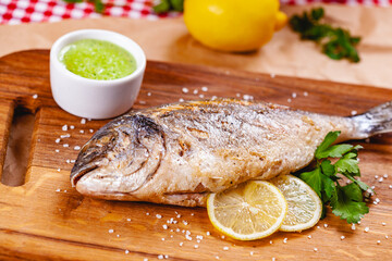 Grilled dorado fish with lemon and sauce on wooden board. Close up