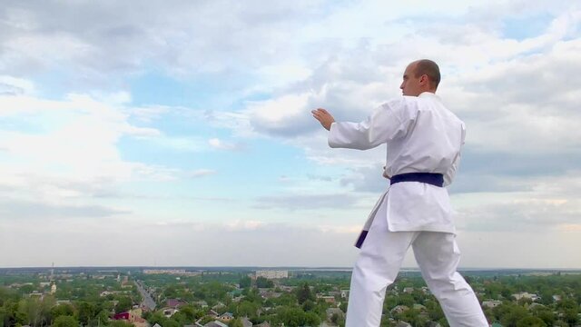 The athlete trains punches and kicks against the sky with clouds