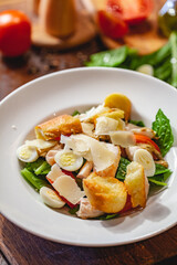 Caesar salad with chicken breast, eggs, croutons, parmesan cheese on white plate. Close up