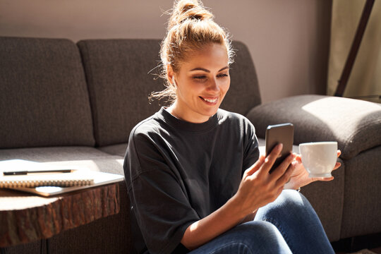 Contented lady smiling while using her smartphone at home