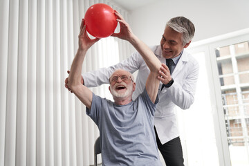 Happy aged man lifting ball with physician help