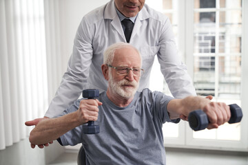 Smiling old man doing upper body workout with rehabilitator