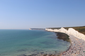 large white rocks by the ocean and blue sky, beach with relax people and green meadows