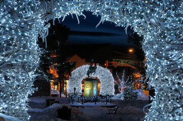 Brightly lit Elk antler arches in Jackson Wyoming town square in winter at twilight with cowboy on bucking broncho statue