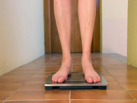 Woman on scales. Female stepping on weighing scales. Feet measuring body weight or overweight, close up