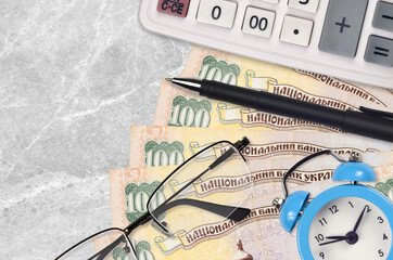 100 Ukrainian hryvnias bills and calculator with glasses and pen. Business loan or tax payment...