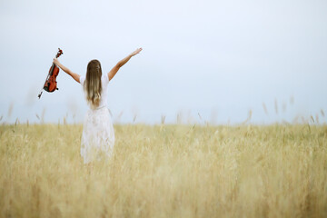 Romantic young woman with flowing hair holding a violin in her hand in a field