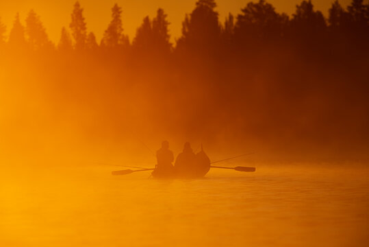 Salmon fishing with rowboat at the sunrise light on misty morning in the Tornio river in Finnish Lapland in June 2020.