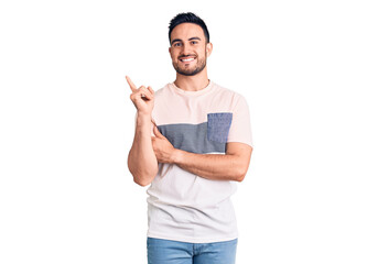 Young handsome man wearing casual clothes with a big smile on face, pointing with hand and finger to the side looking at the camera.