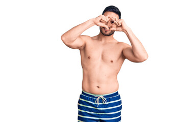 Fototapeta premium Young handsome man wearing swimwear doing heart shape with hand and fingers smiling looking through sign