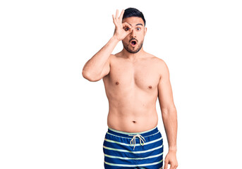 Fototapeta premium Young handsome man wearing swimwear doing ok gesture shocked with surprised face, eye looking through fingers. unbelieving expression.