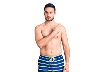 Fototapeta premium Young handsome man wearing swimwear pointing with hand finger to the side showing advertisement, serious and calm face