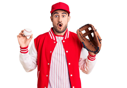 Young handsome man holding baseball gloves scared and amazed with open mouth for surprise, disbelief face