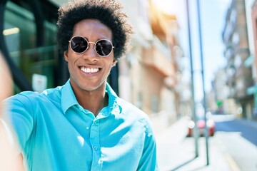 Young handsome african american man wearing casual clothes and sunglasses smiling happy. Making selfie by the camera at town street.