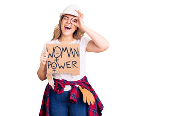 Young caucasian woman holding woman power banner smiling happy doing ok sign with hand on eye looking through fingers