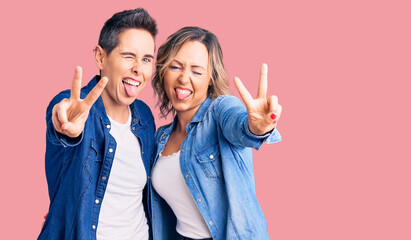 Couple of women wearing casual clothes smiling with tongue out showing fingers of both hands doing victory sign. number two.