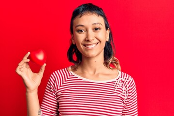Young woman holding heart looking positive and happy standing and smiling with a confident smile showing teeth