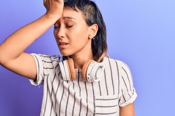 Fototapeta premium Young woman listening to music using headphones surprised with hand on head for mistake, remember error. forgot, bad memory concept.