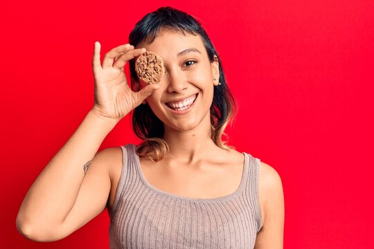 Young woman holding cookie looking positive and happy standing and smiling with a confident smile showing teeth