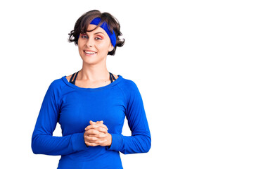Beautiful young woman with short hair wearing training workout clothes with hands together and crossed fingers smiling relaxed and cheerful. success and optimistic
