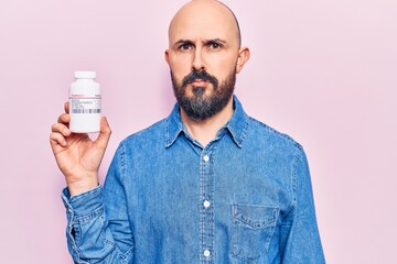 Young handsome man holding pills thinking attitude and sober expression looking self confident