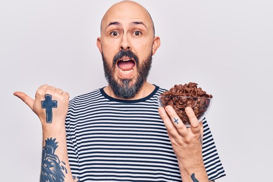 Young handsome man holding chocolate cereals pointing thumb up to the side smiling happy with open mouth