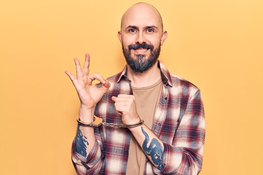 Young handsome man wearing prisoner handcuffs doing ok sign with fingers, smiling friendly gesturing excellent symbol