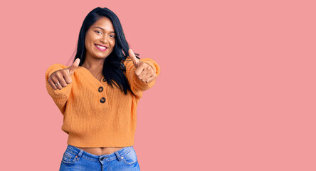 Hispanic woman with long hair wearing casual winter sweater approving doing positive gesture with hand, thumbs up smiling and happy for success. winner gesture.