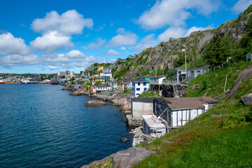 Fototapeta na wymiar St. John's, NL / Canada - July 2020: Houses along the hillside of St. John's Harbour. The houses are colorful and stacked on top of each other. The water is bright blue. The sky is blue and cloudy. 