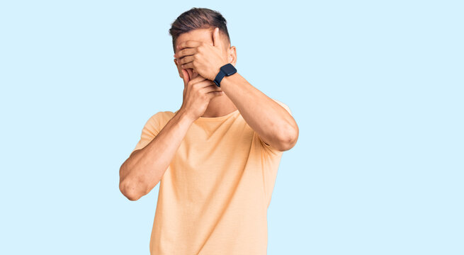 Young handsome man wearing casual clothes covering eyes and mouth with hands, surprised and shocked. hiding emotion