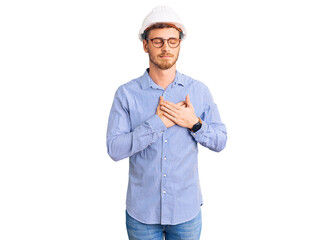 Handsome young man with bear wearing architect hardhat smiling with hands on chest with closed eyes and grateful gesture on face. health concept.