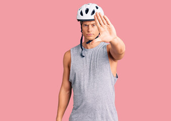 Young handsome man wearing bike helmet doing stop sing with palm of the hand. warning expression with negative and serious gesture on the face.