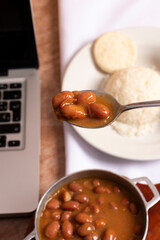 Frijoles en mesa de trabajo en casa para almorzar con arroz arepa y aguacate. Plato tradicional para comer mientras trabajamos en casa cuchara a punto de comer frijoles rojos