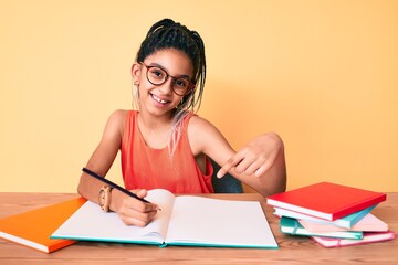 Young african american girl child with braids studying for school exam smiling happy pointing with hand and finger