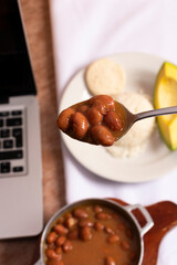Frijoles en mesa de trabajo en casa para almorzar con arroz arepa y aguacate. Plato tradicional para comer mientras trabajamos en casa cuchara a punto de comer frijoles rojos