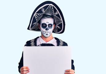 Young man wearing day of the dead costume holding blank empty banner thinking attitude and sober expression looking self confident