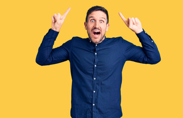 Fototapeta premium Young handsome man wearing casual shirt smiling amazed and surprised and pointing up with fingers and raised arms.