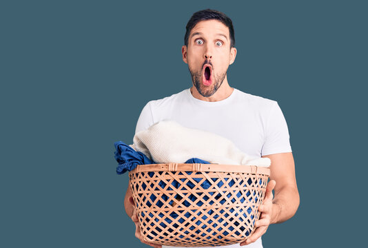 Young handsome man holding laundry basket scared and amazed with open mouth for surprise, disbelief face