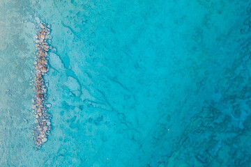 An aerial view of the beautiful Mediterranean sea, where you can see a vertical textured line of rocks underwater on the left side and the clean turquoise water of Cyprus