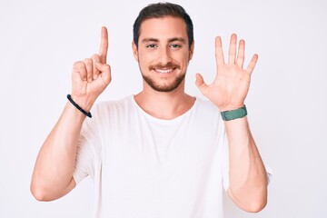Fototapeta premium Young handsome man wearing casual white tshirt showing and pointing up with fingers number six while smiling confident and happy.